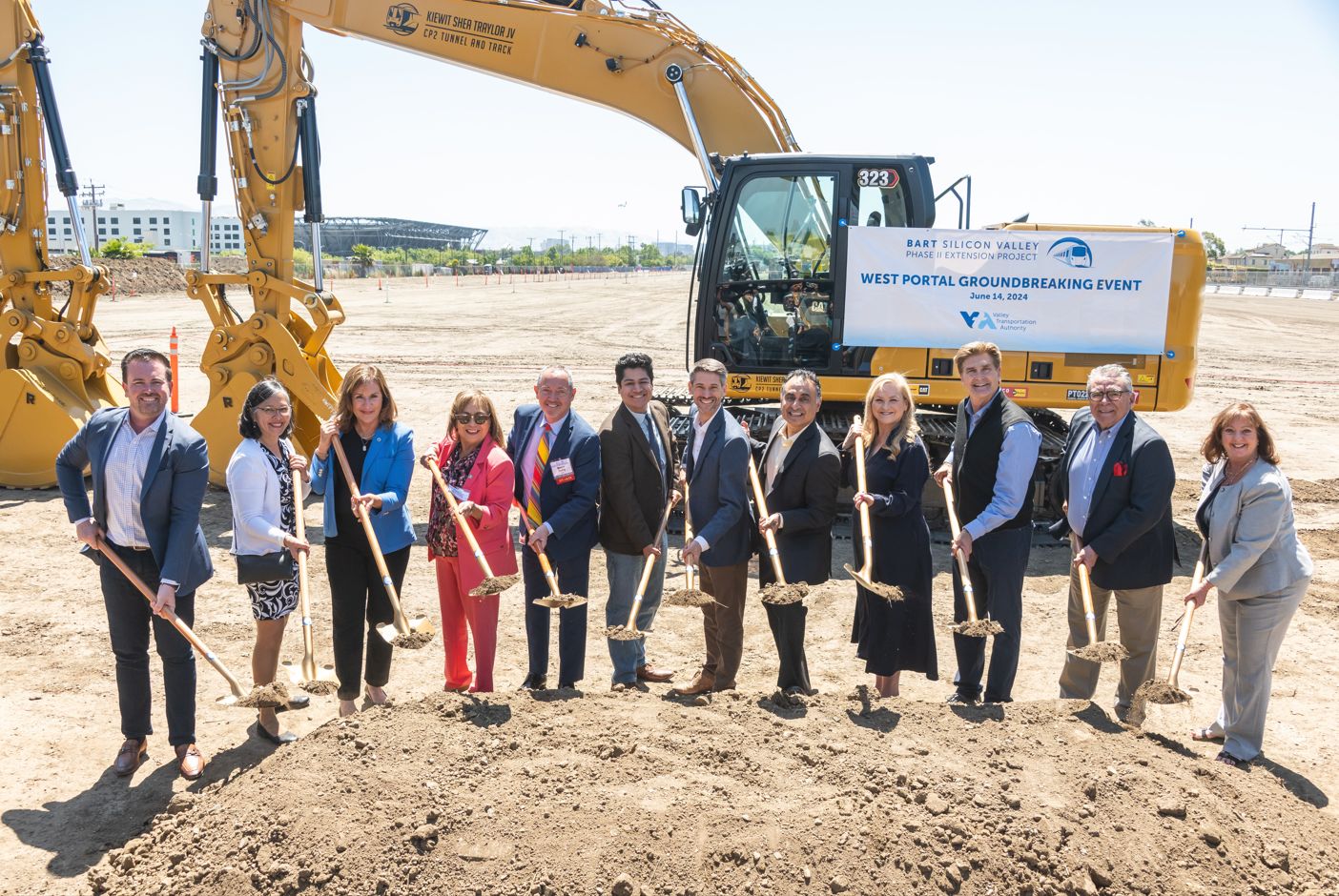 group of professionals hold shovels and stand in front of yellow tractor