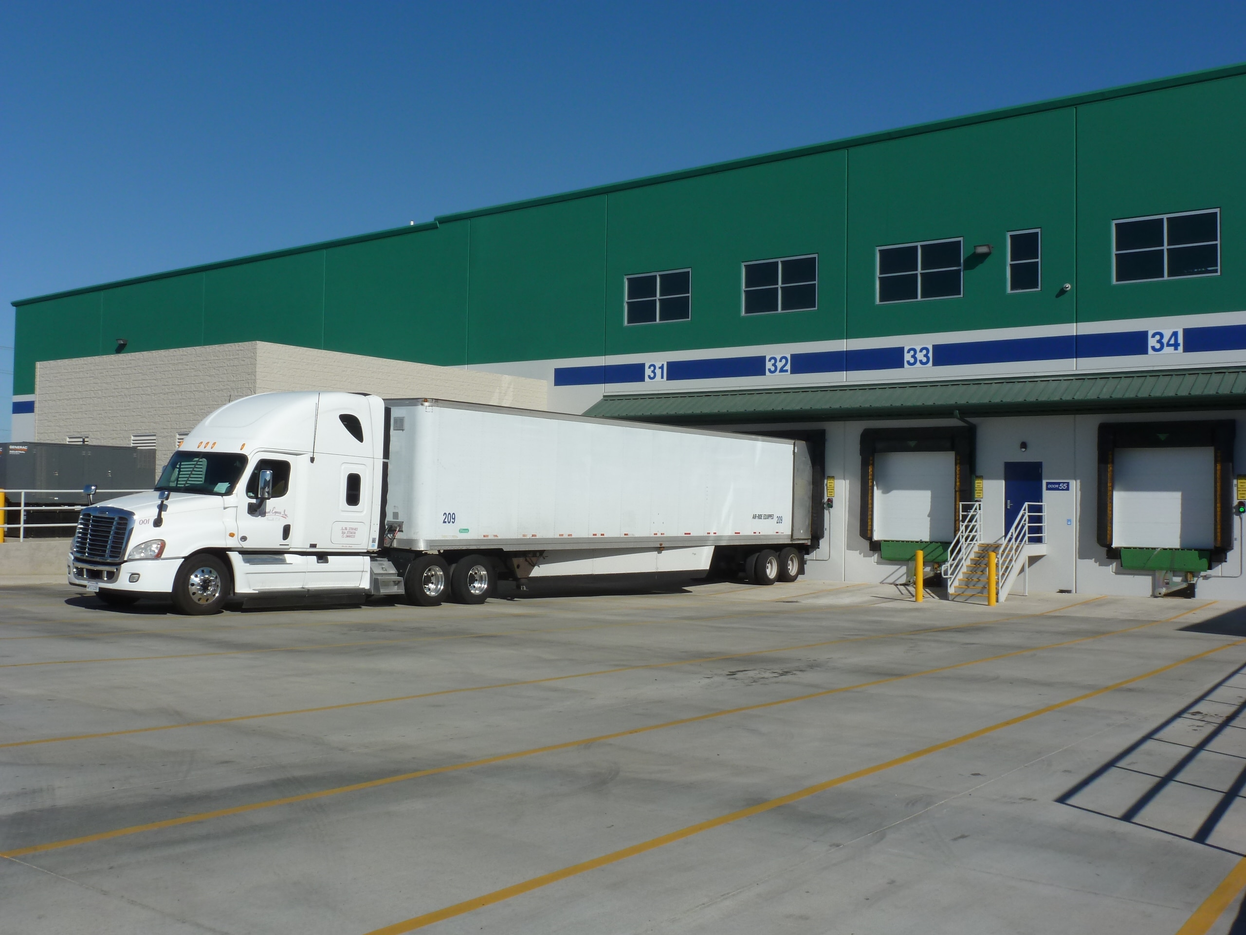 a white semi truck is backed into a large, green distribution facility