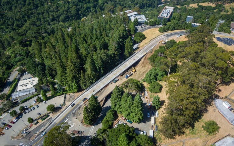 road travels along tree covered hillside leading to a parking lot and buildings